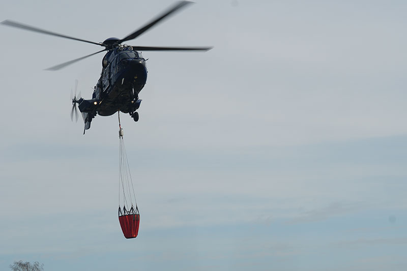 Bild: Foto eines Hubschraubers mit einem Bambi Bucket im Anflug