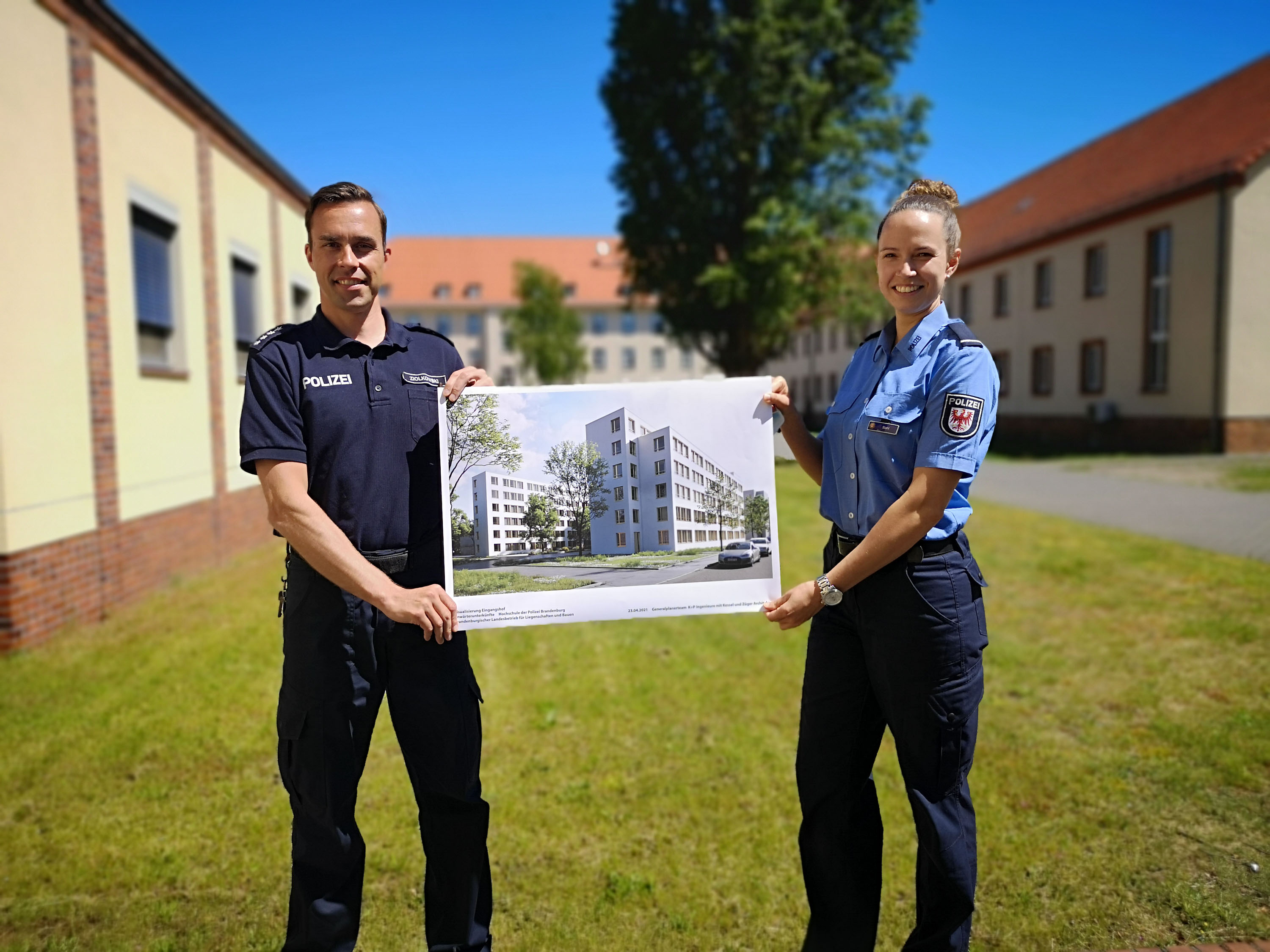 Bild: Foto von zwei Polizeibeamten, die auf einer Tafel eine Visualisierung des neuen Anwärterwohnheims an der HPol Brandenburg prräsentieren