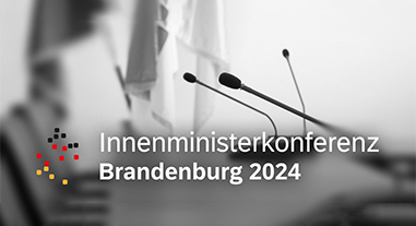 Foto von einem Beratungstsich mit Tischmikrofonen und dem Logo der IMK Brandenburg 2024 im Vordergrund