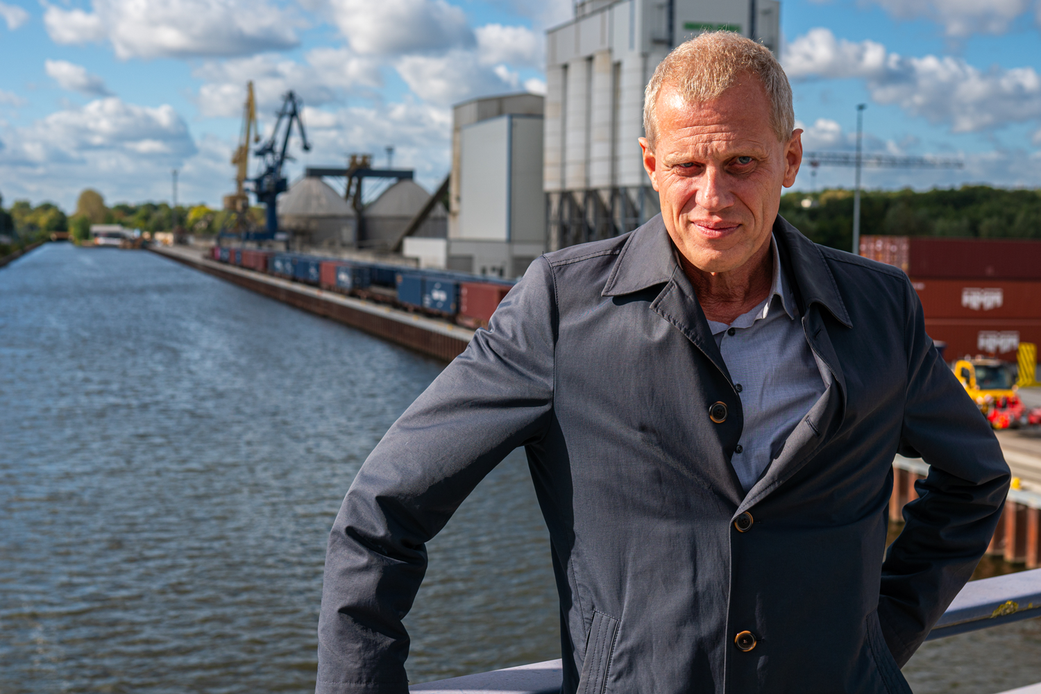 Bild: Hafen-Geschäftsführer steht auf Brücke und hat im Hintergrund eine Hafenansicht mit Kanal